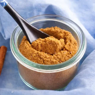 Low FODMAP Curry Spice Mix in a glass jar with spoon and whole spices.