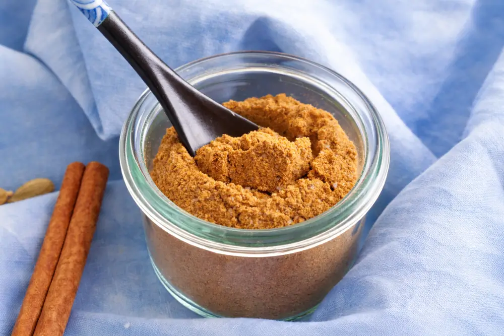 Low FODMAP Curry Spice Mix in a glass jar with spoon and whole spices.