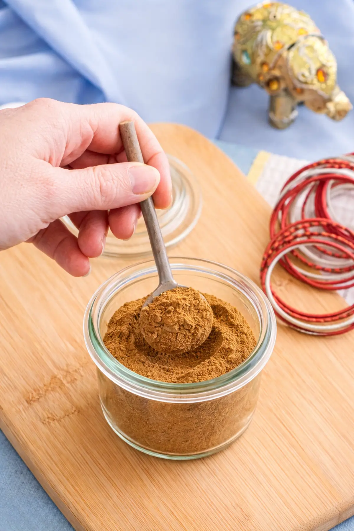 Low FODMAP garam masala in a small glass jar with a spoon lifting the spice.