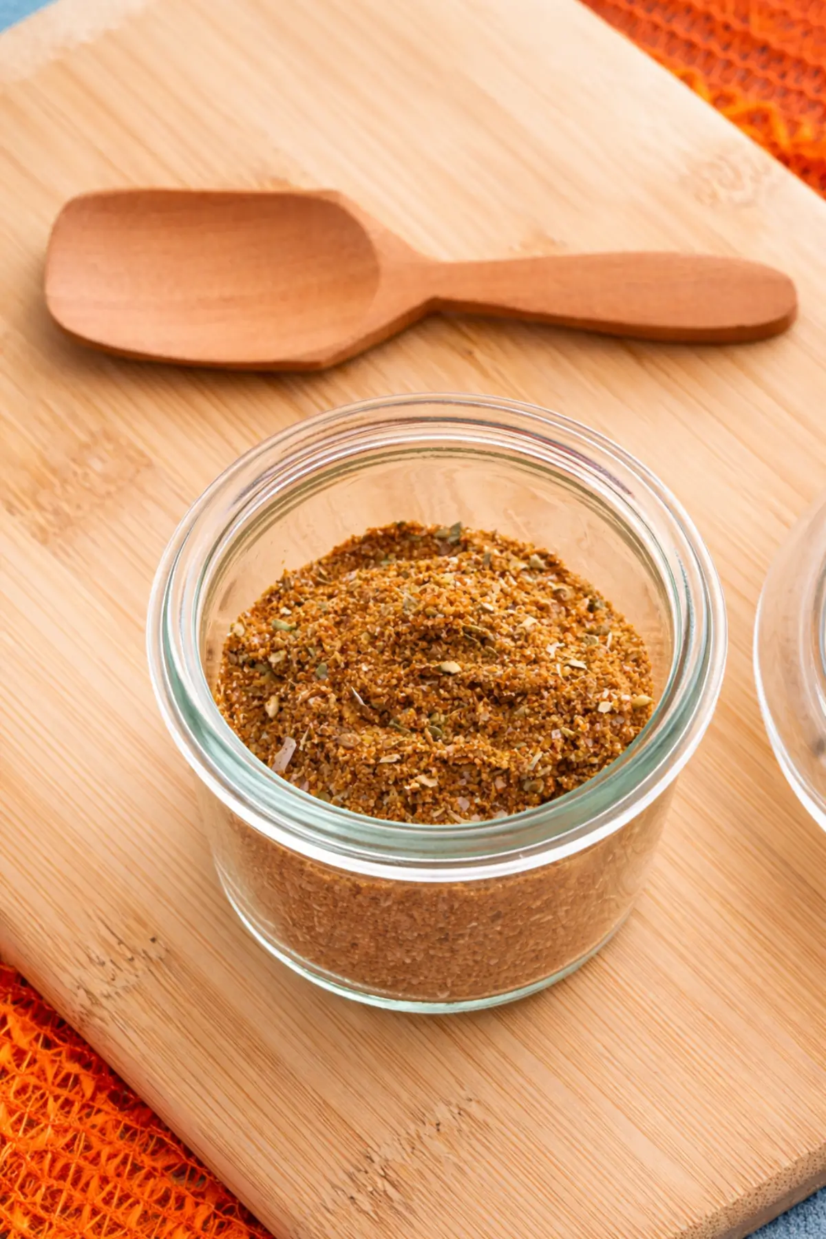 Low FODMAP taco seasoning in a glass jar with spoon on a wooden board.