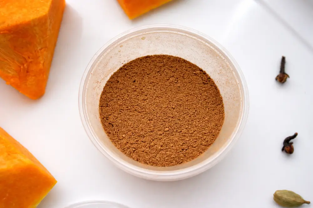 Pumpkin pie spice in a glass jar with cinnamon sticks and cardamom pods.