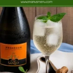 Hugo cocktail served with mint garnish, ice, and sparkling bubbles in a wine glass.