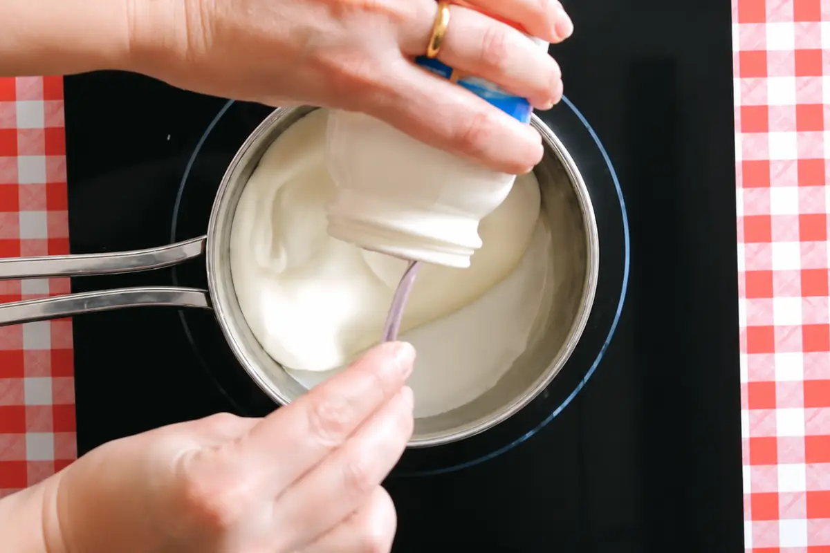 Cream and milk being stirred in a pot for panna cotta.