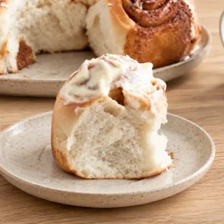 Close-up of a golden cinnamon roll topped with thick cream cheese frosting and a torn front section.