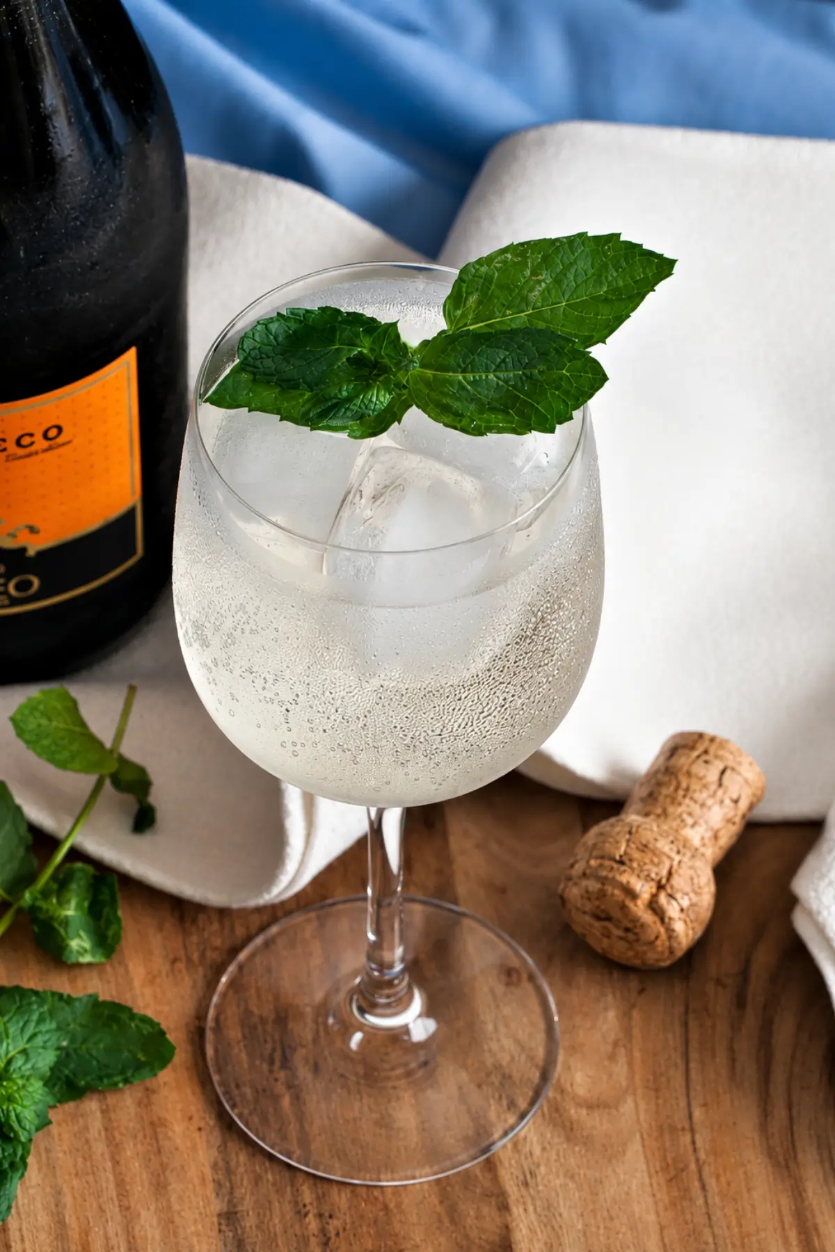 Elderflower spritz with fresh mint, ice cubes, and a bottle of Prosecco beside the glass.