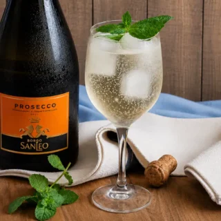 Hugo cocktail served with mint garnish, ice, and sparkling bubbles in a wine glass.