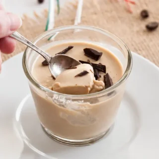Spoon dipping into coffee panna cotta topped with chopped chocolate.