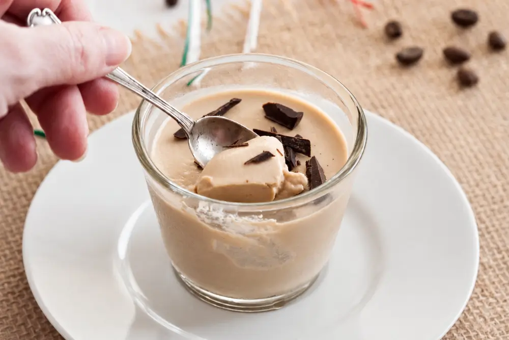 Spoon dipping into coffee panna cotta topped with chopped chocolate.