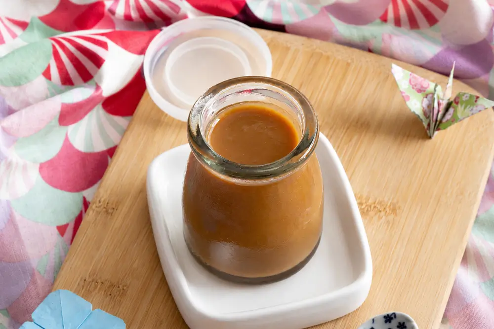 Jar of homemade Miso Caramel Sauce on a small white tray.