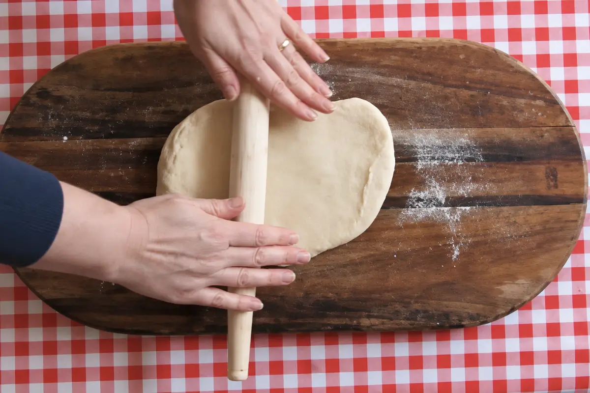 Rolling Sourdough Grissini dough into a thick rectangle on a wooden board before rising.