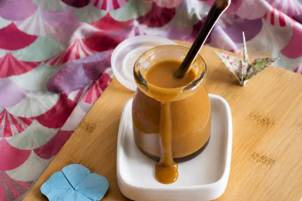 Spoon standing in a jar of silky Miso Caramel Sauce.