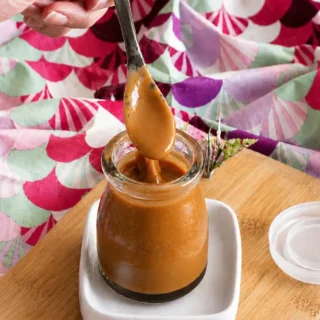 Spoon coated with silky Miso Caramel Sauce over a glass jar.