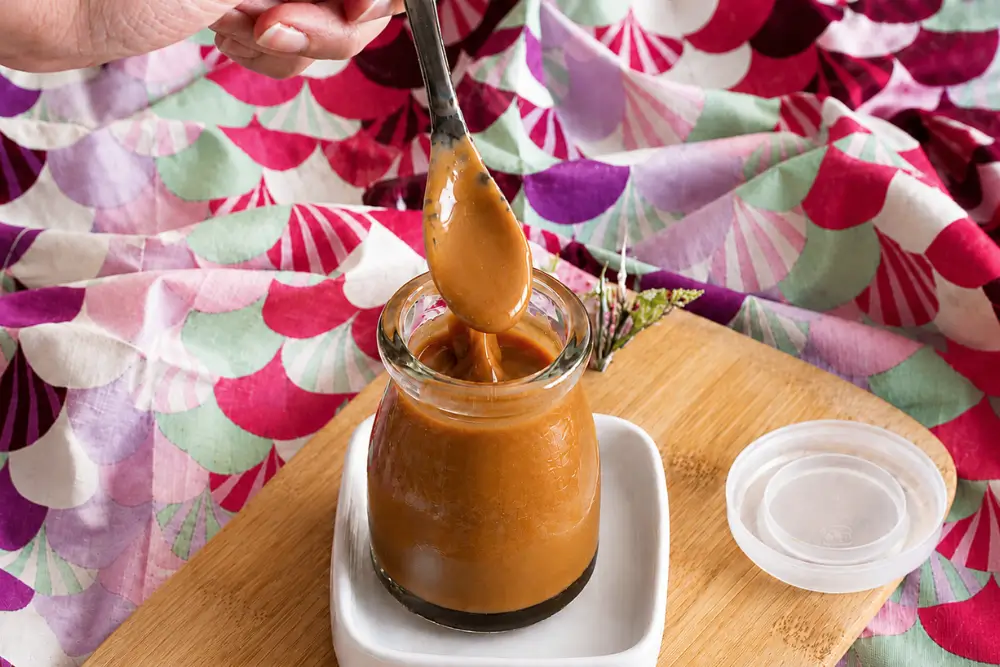 Spoon coated with silky Miso Caramel Sauce over a glass jar.