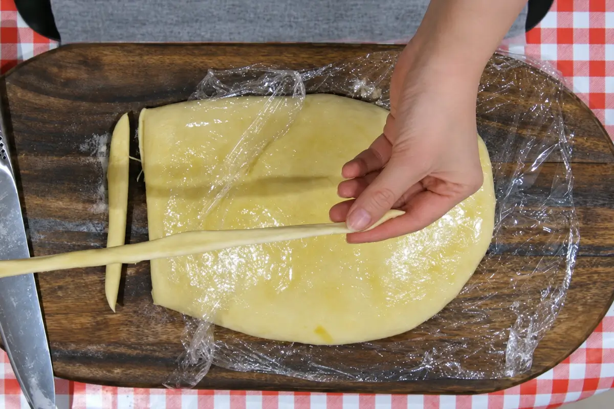 Gently stretching a strip of dough by hand to form a long Sourdough Grissini breadstick.
