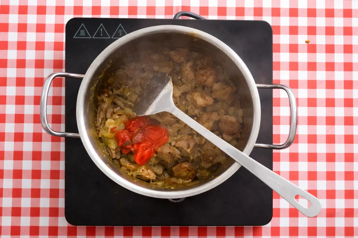 Tomato paste being added to browned beef with spices in a pot.
