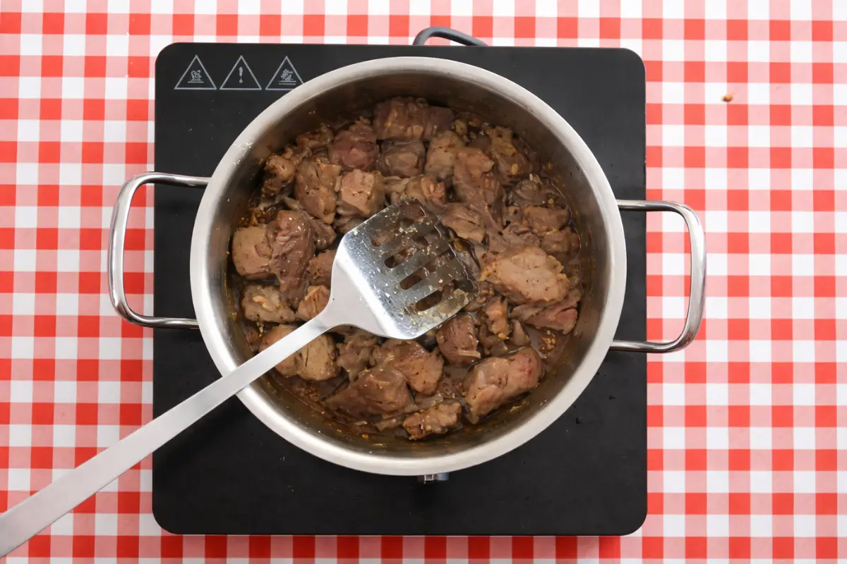 Beef browning in a pot with oil, developing colour on the surface.