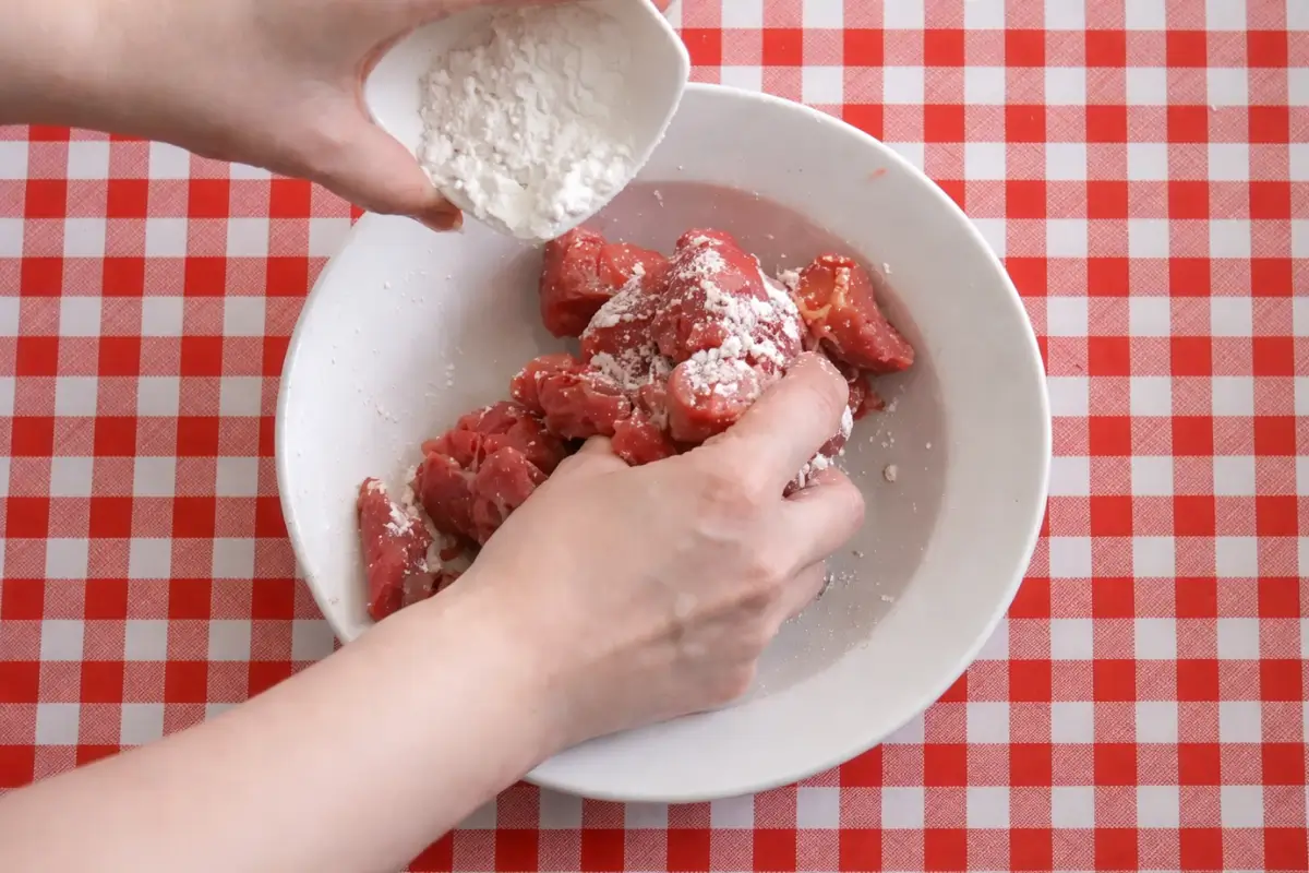 Beef pieces being coated with flour in a bowl before cooking.