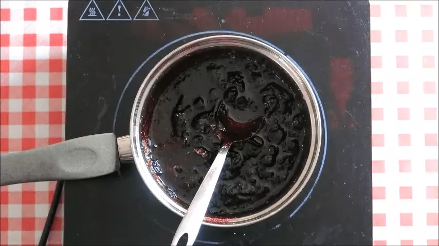 Blueberry jam simmering and thickening in a pot while being stirred on the stovetop.