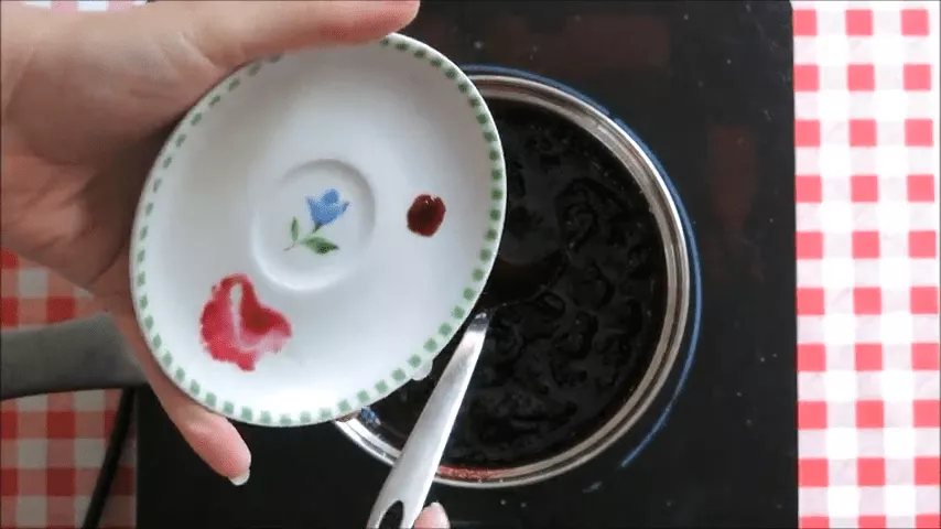 Checking if the blueberry jam has set by testing a small drop on a chilled plate.