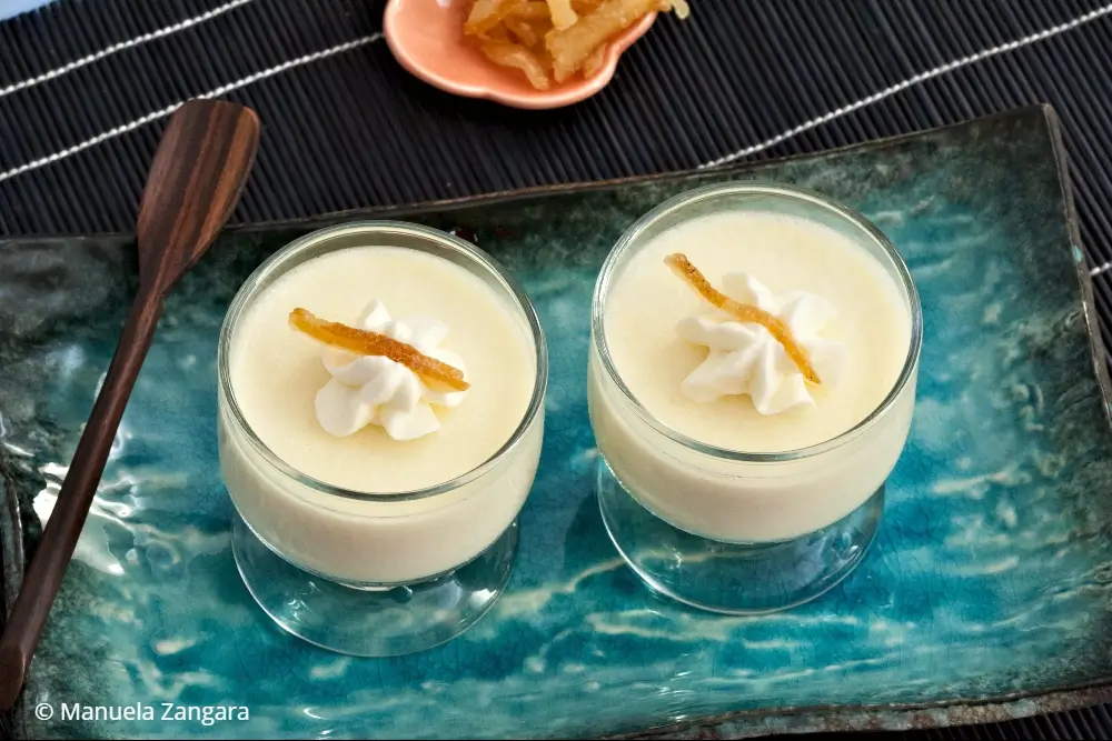 Close-up of two yuzu panna cotta cups with whipped cream and citrus peel.