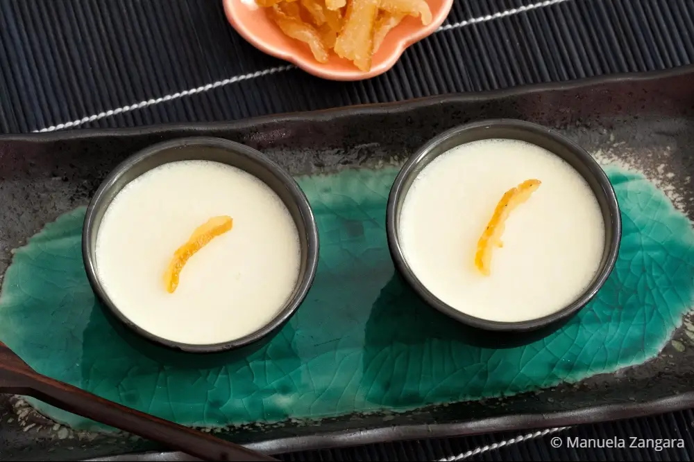 Two small bowls of yuzu panna cotta topped with a strip of citrus peel.
