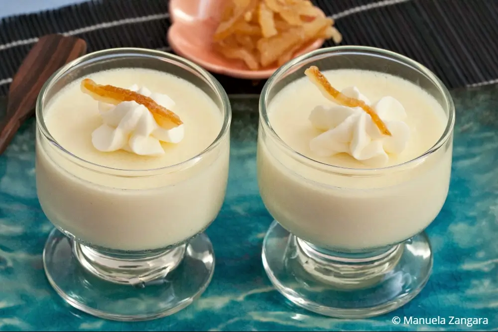Two glasses of yuzu panna cotta topped with whipped cream and candied peel.