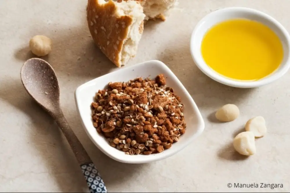 Bowl of dukkah with torn bread and olive oil on the side.
