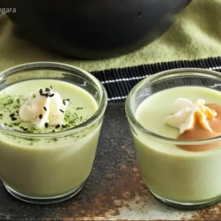 Pair of matcha panna cottas served in glass cups with cream and toppings.