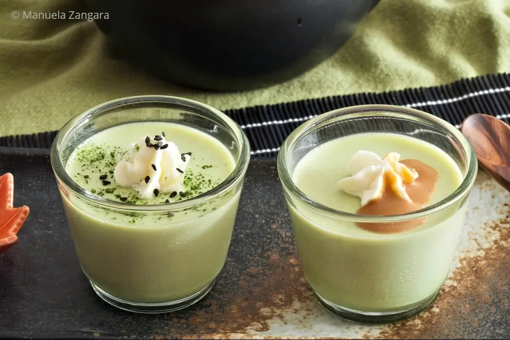 Pair of matcha panna cottas served in glass cups with cream and toppings.