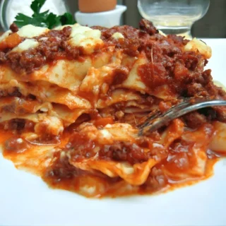Lasagne layered with meat ragù and creamy béchamel sauce served on a white plate.