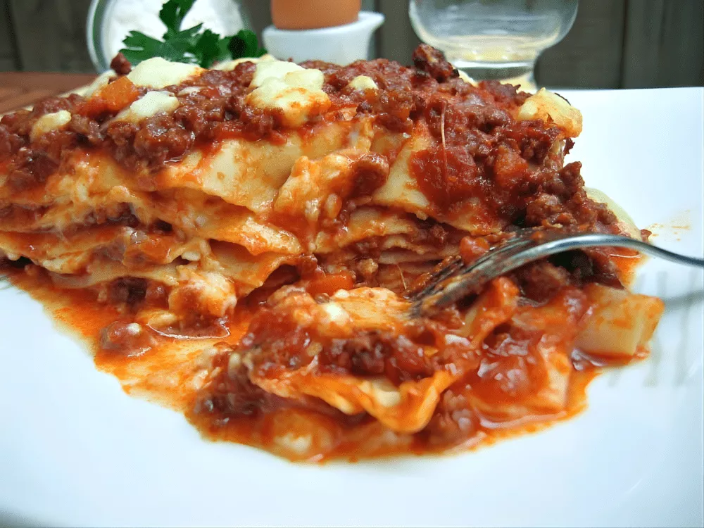 Lasagne layered with meat ragù and creamy béchamel sauce served on a white plate.