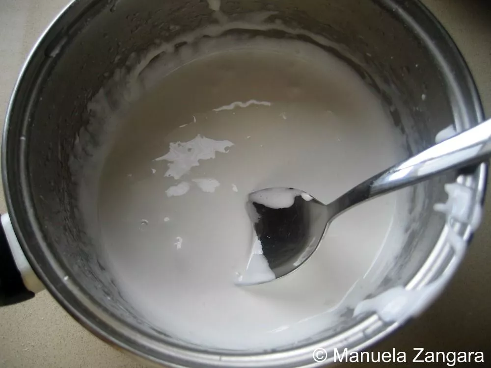 Homemade royal icing being mixed with a spoon to a smooth consistency.