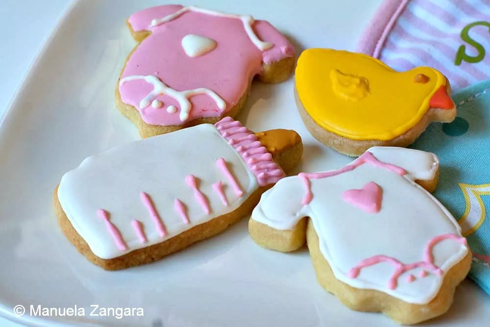 Baby shower cookies decorated with royal icing shaped like bottles, ducks and onesies.