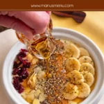 Maple syrup being poured over yoghurt topped with banana slices, seeds and nuts.