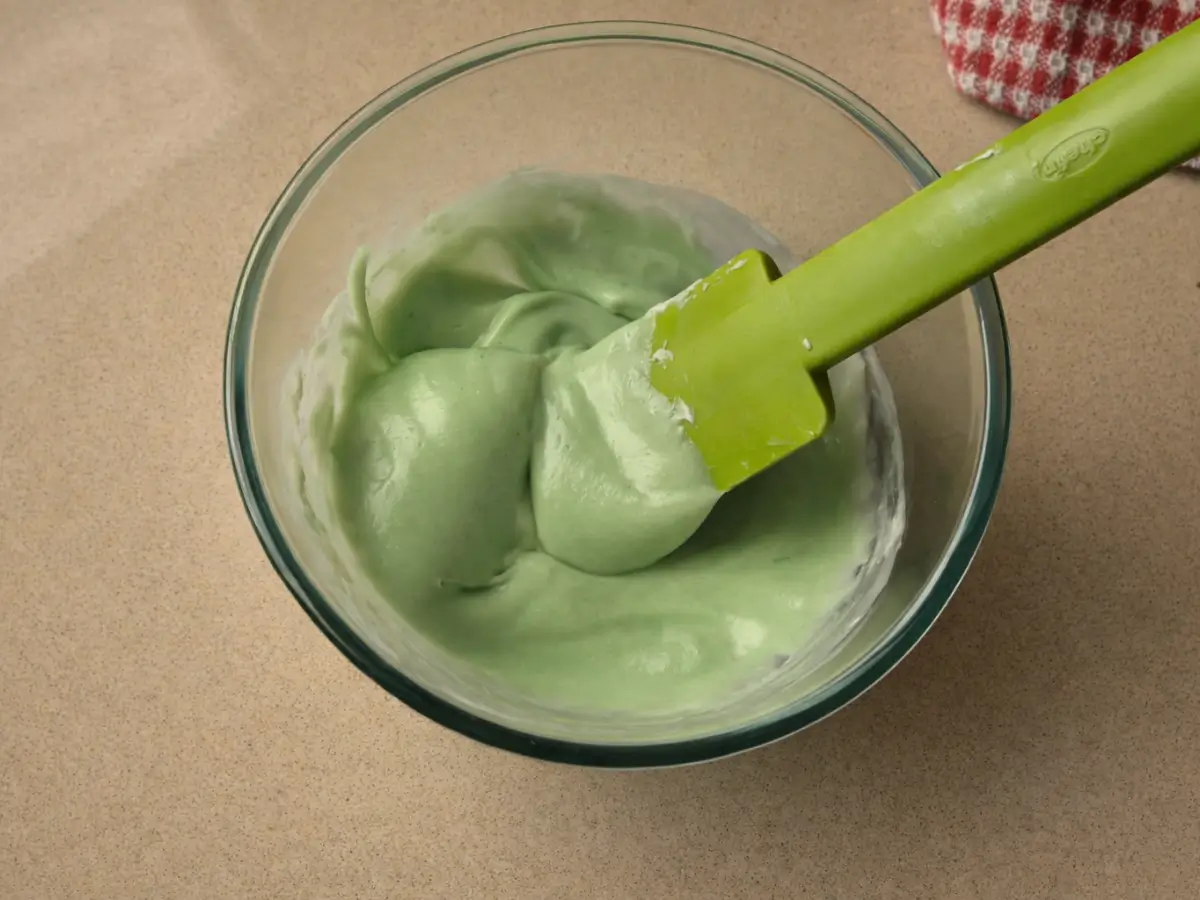 Adding peppermint extract to melted white chocolate mixture in bowl.