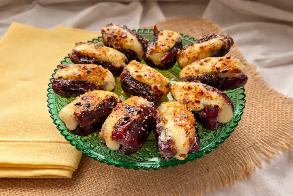 Brie stuffed dates with caramelised sugar topping served on a green plate.
