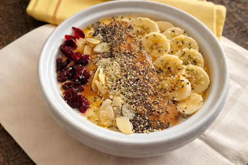 Finished yoghurt bowl with banana, almond butter, seeds and dried cranberries on a linen cloth.