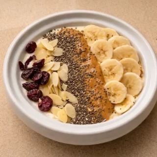 Banana Nut Greek Yogurt Bowl topped with banana, almond butter, seeds and maple syrup in a white bowl.