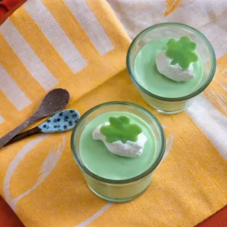 Two chilled mint mousse cups with whipped cream and shamrock toppers.