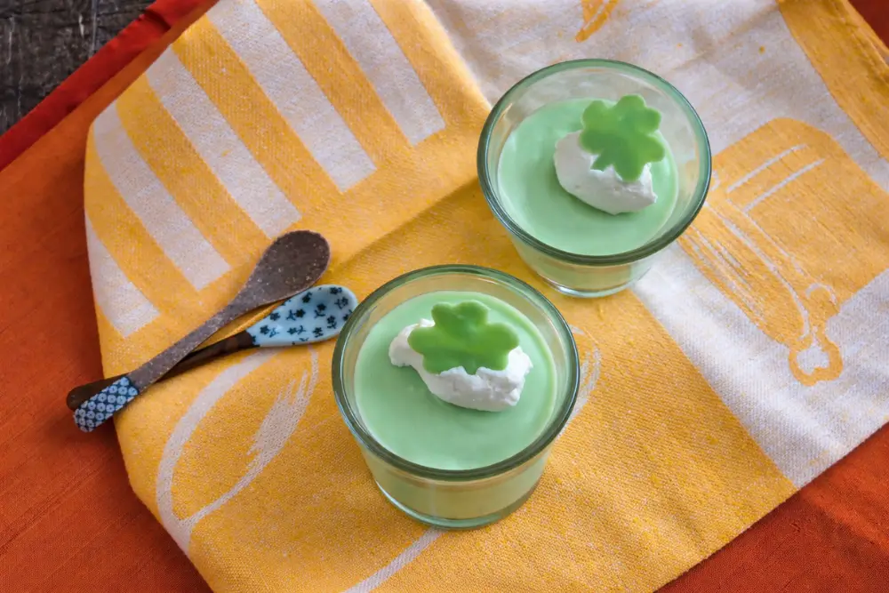 Two chilled mint mousse cups with whipped cream and shamrock toppers.