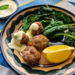 Lamb and Mint Meatballs with Lemon Yogurt Sauce served on a plate with fresh spinach and a lemon wedge.
