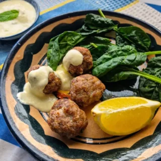 Lamb and Mint Meatballs with Lemon Yogurt Sauce served on a plate with fresh spinach and a lemon wedge.