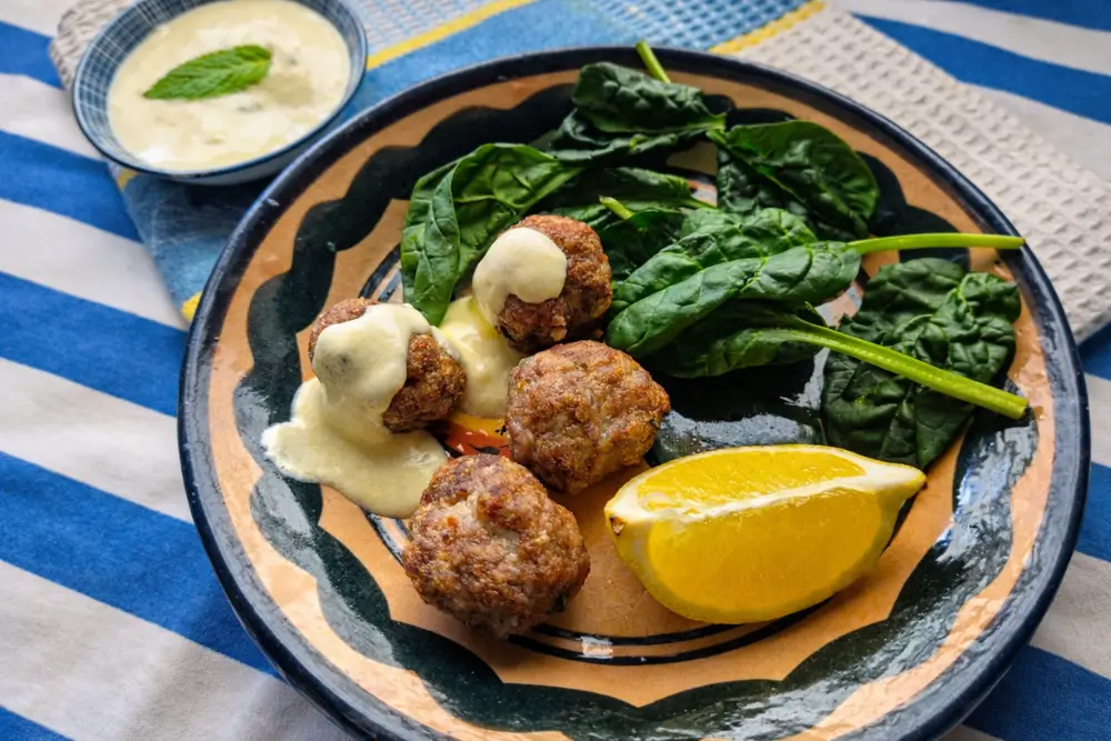 Lamb and Mint Meatballs with Lemon Yogurt Sauce served on a plate with fresh spinach and a lemon wedge.