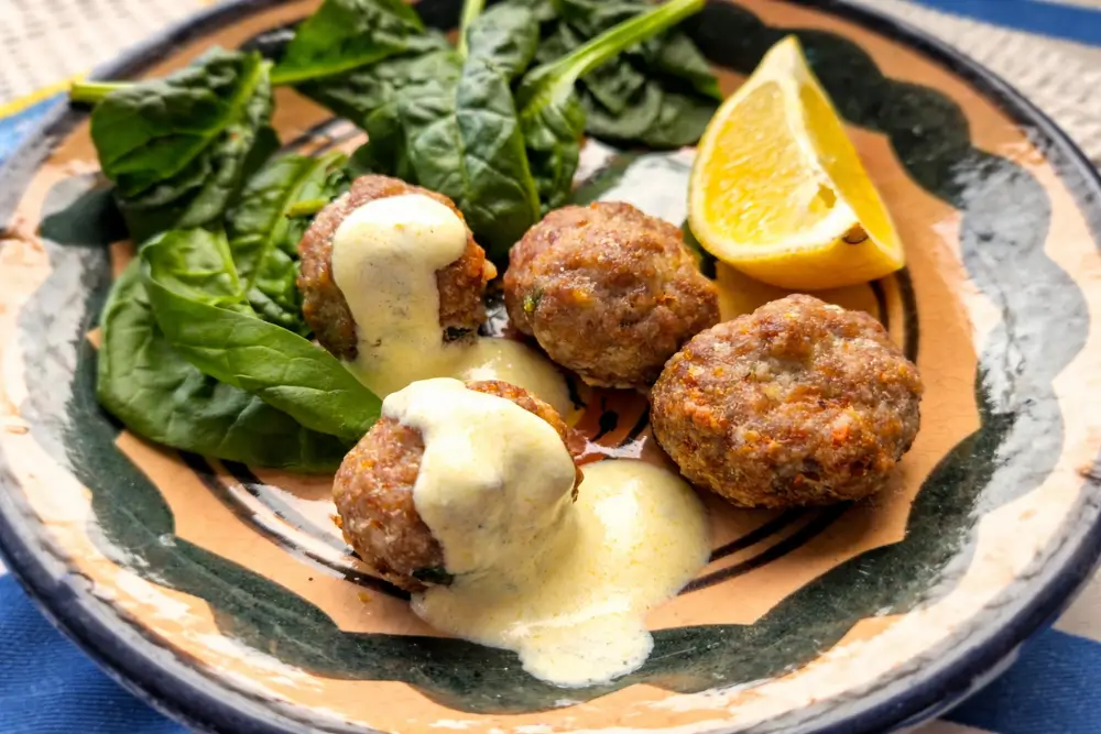Lamb meatballs with mint on spinach, drizzled with lemon yoghurt sauce and served with a lemon wedge.