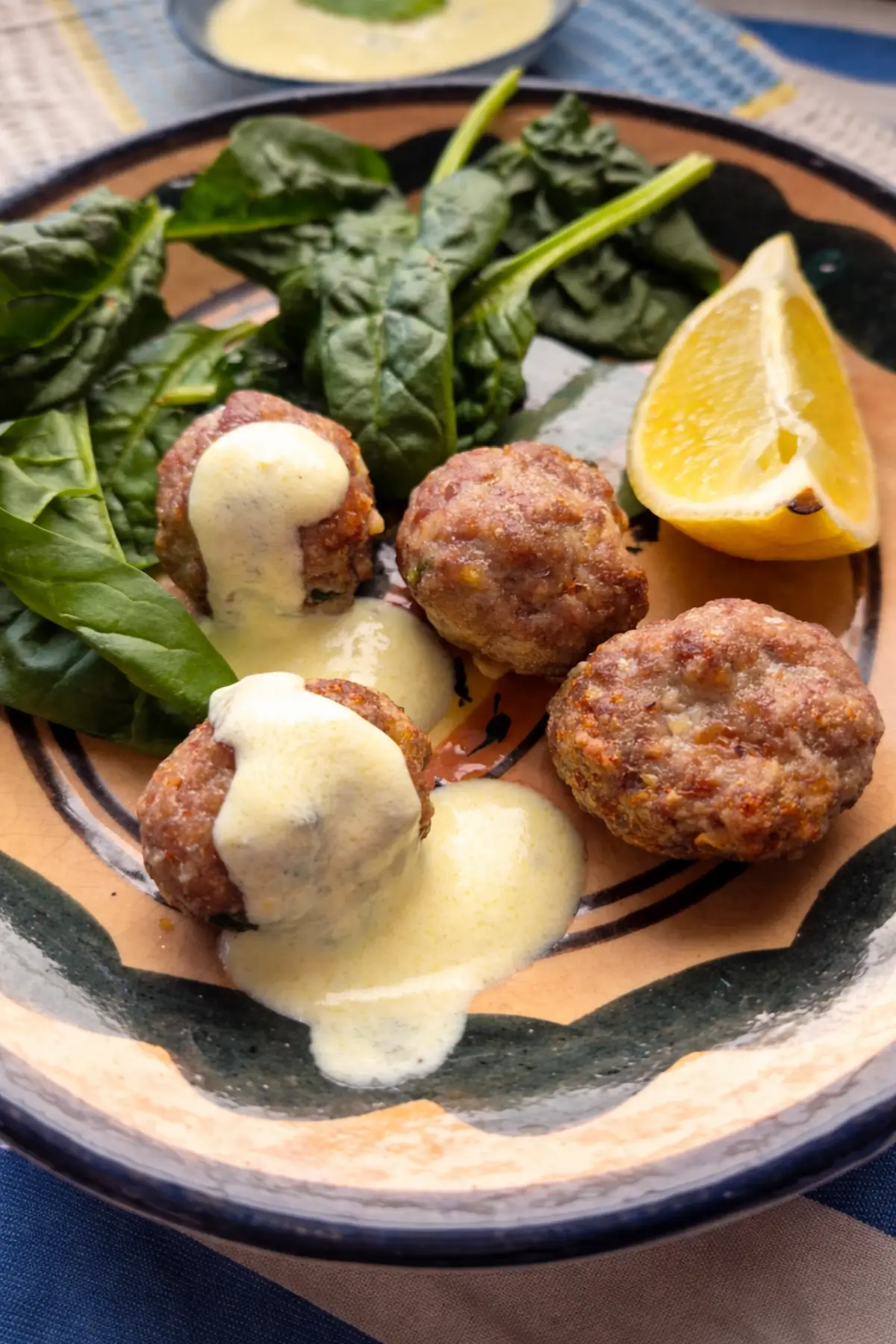 Cooked lamb meatballs with mint topped with lemon yoghurt sauce and served with spinach and a lemon wedge.