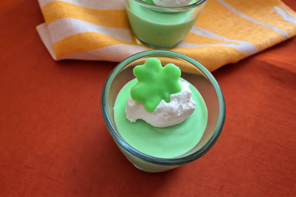 Close-up of mint mousse in a glass with whipped cream and green shamrock.