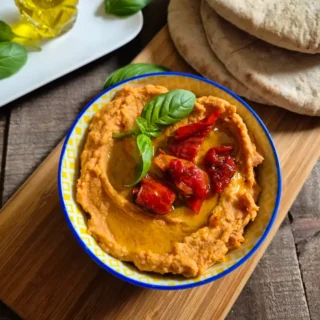 Sun-Dried Tomato Hummus served in a bowl with pita bread and olive oil on a wooden board.
