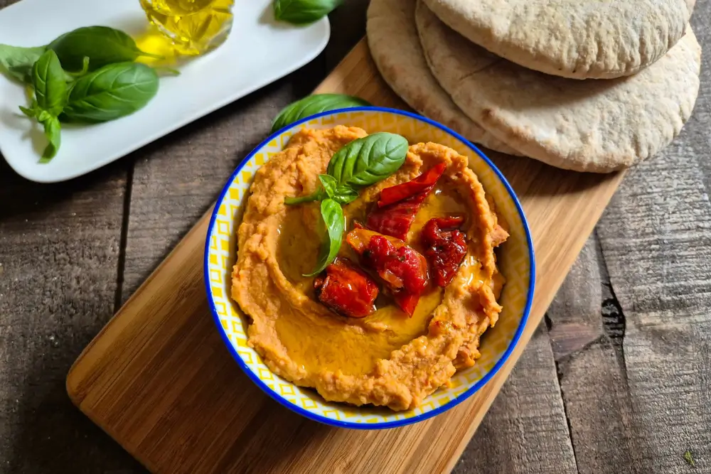 Sun-Dried Tomato Hummus served in a bowl with pita bread and olive oil on a wooden board.