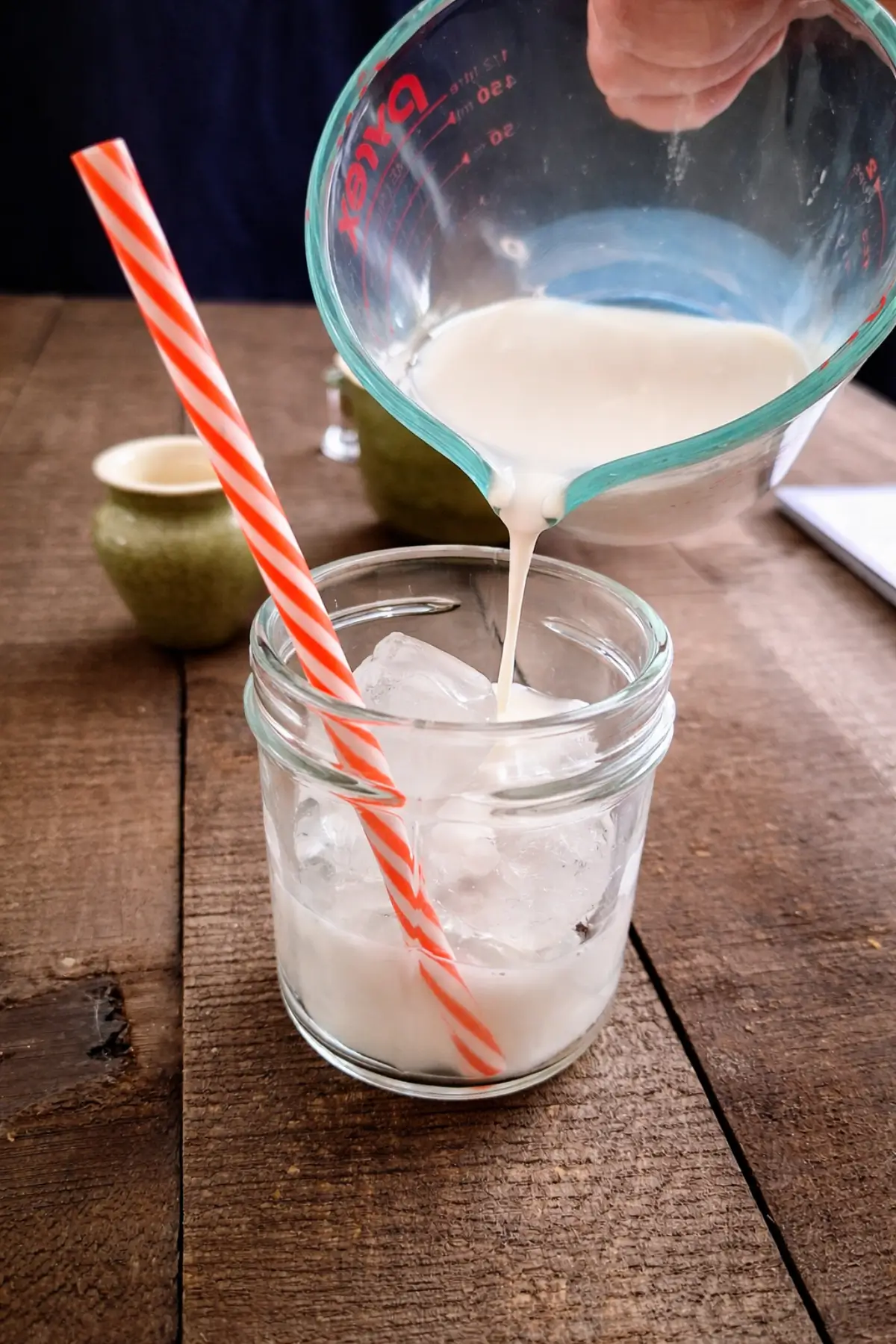 Milk being poured over ice cubes in a glass before adding matcha.
