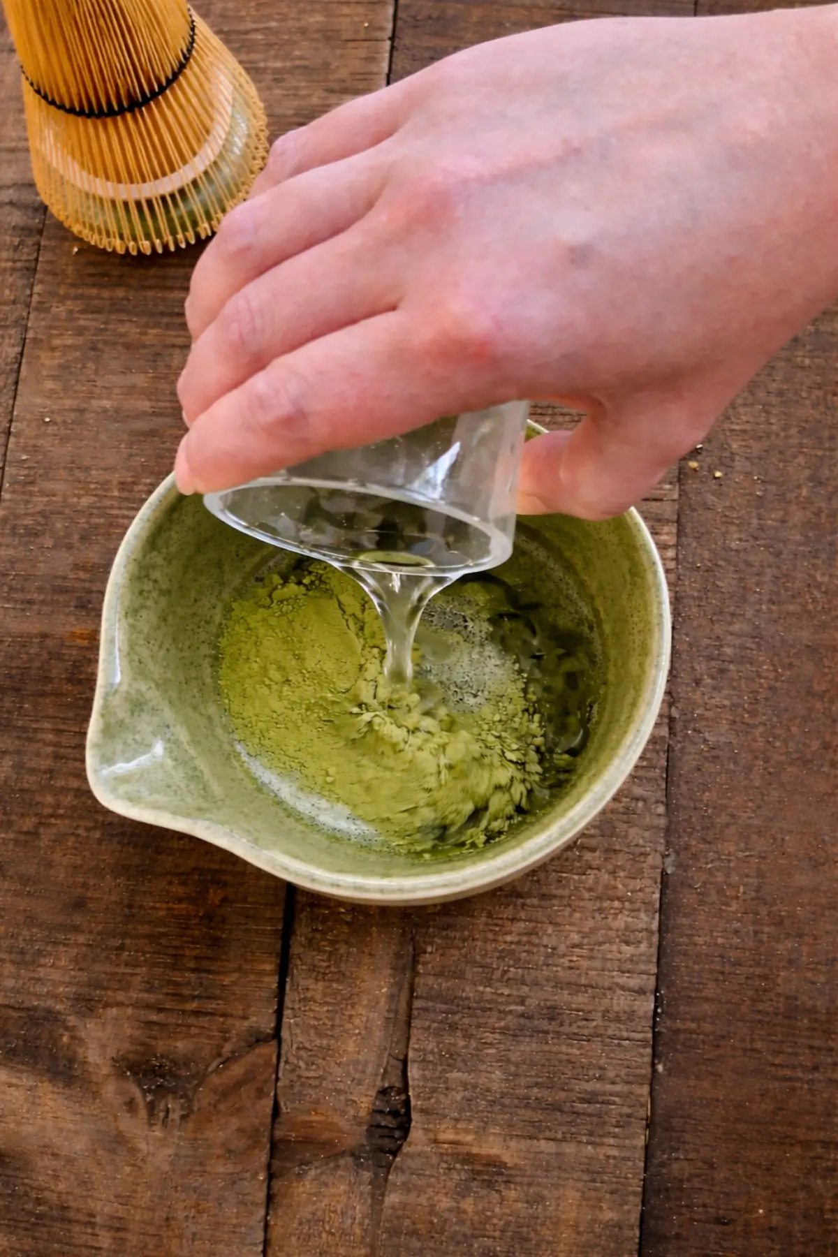 Hot water being added to matcha powder in a bowl with a pouring spout.